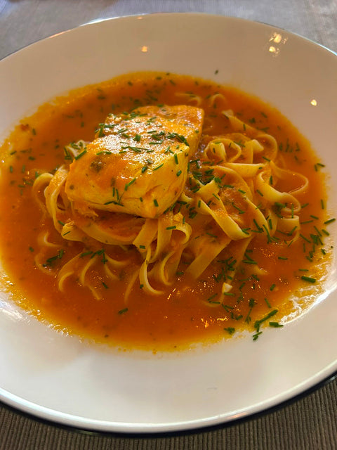 Photograph of a bowl of KATZ summer saffron-tomato fish soup, garnished with fresh chives