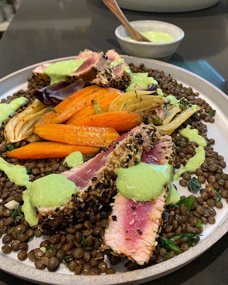 Seared ahi tuna, crusted with seeds and dried spices, on a bed of lentils and roasted vegetables and drizzled with a green tahini sauce 